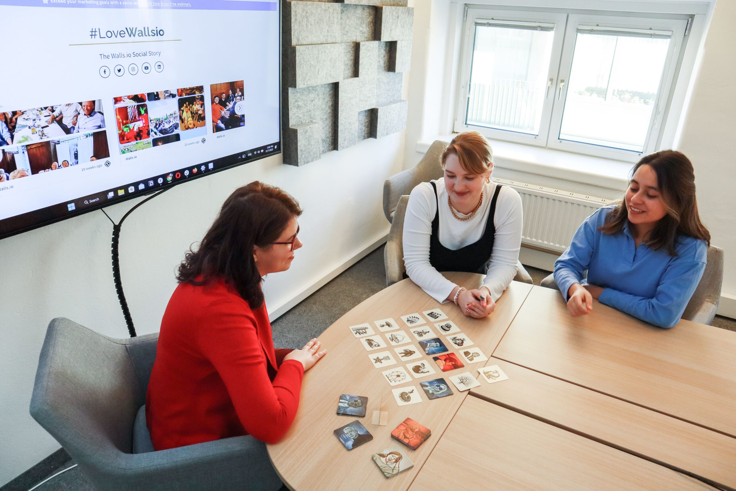 Three women playing a card game in a modern office setting, enjoying team building time.