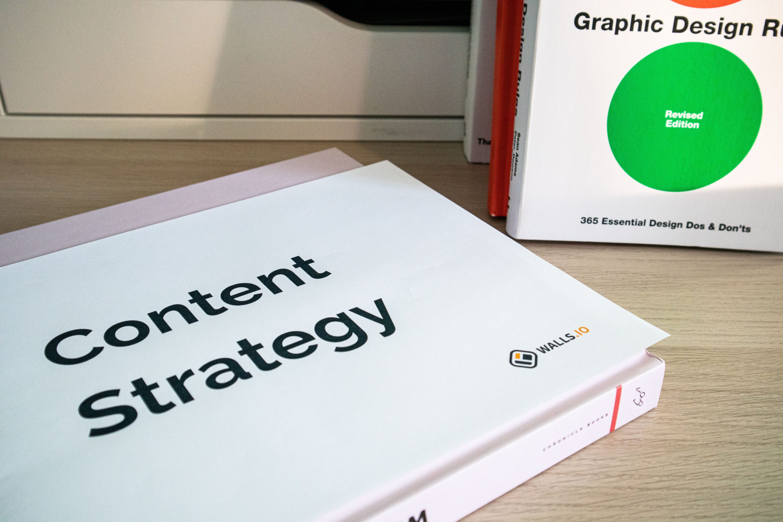 Books on content strategy and graphic design essentials resting on a wooden desk.